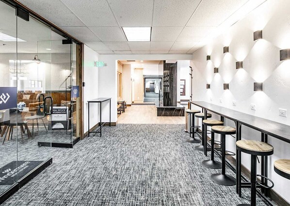 A modern office space with glass walls, a long counter with stools, and a carpeted floor.