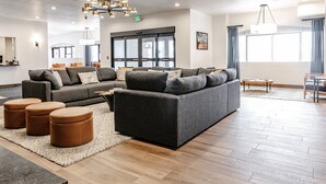 A modern living room with a sectional sofa, ottomans, and a coffee table. There are large windows, a chandelier, and a door with glass panels.