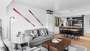 A modern living room with a grey sofa, a wooden coffee table, and a dining area with a kitchen in the background. - Shadow Ridge 300-3 | Walk to Lifts | Mtn Views | Kitchen | Fireplace | Updated | Pool & Hot Tub (Park City)