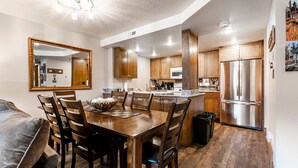 Una cocina moderna con armarios de madera, un refrigerador de acero inoxidable y un comedor con mesa y sillas de madera.