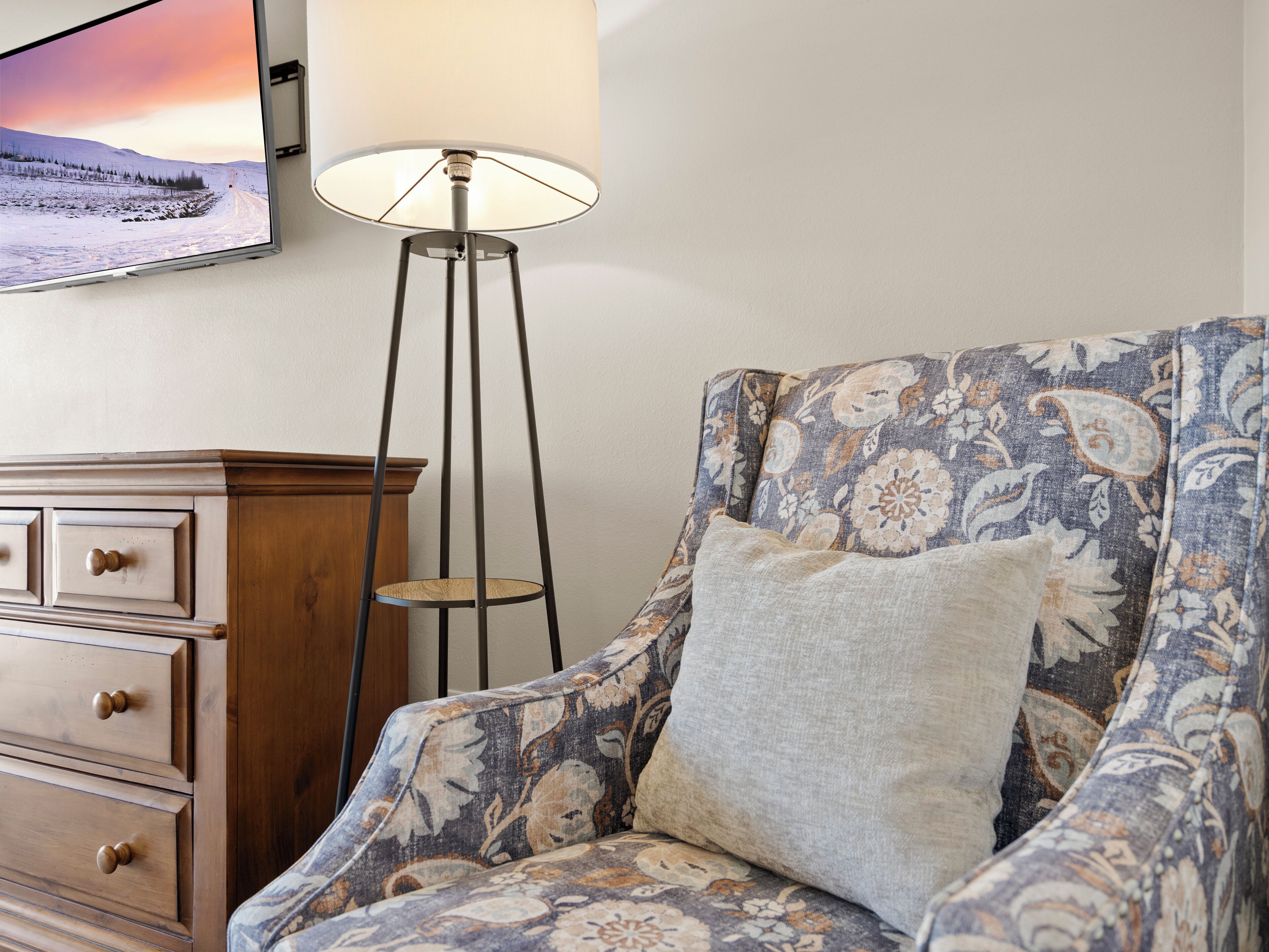 A room with a patterned armchair, a wooden cabinet, and a floor lamp.