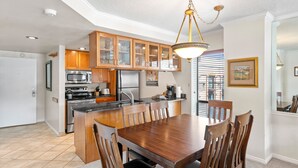 A modern kitchen with wooden cabinets, stainless steel appliances, and a dining area with a wooden table and chairs.