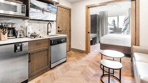 Eine kompakte Küche mit modernen Geräten, ein Essbereich mit zwei Hockern und ein Schlafzimmer mit Blick auf schneebedeckte Bäume.