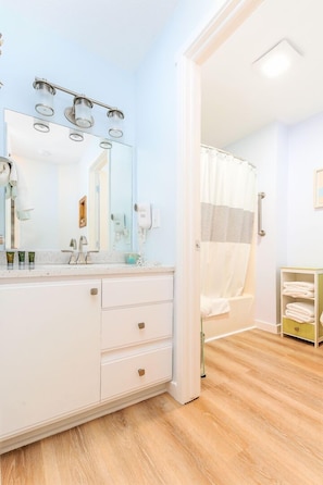 A bathroom with a white vanity, a large mirror, a shower curtain, and a towel rack.