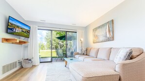Una sala de estar moderna con sofá, televisor y vistas a un jardín a través de grandes puertas correderas de vidrio.