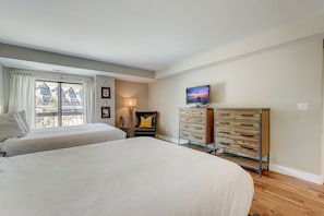 A bedroom with two beds, a dresser, a TV, and a window with curtains.