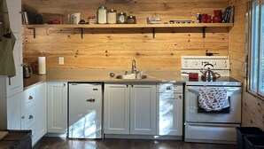 A wooden cabin-style kitchen with a wooden ceiling, white cabinets, a sink, a stove, and a window. - Waterfront Cottage for Rent in Parry Sound Region 
 (Pointe au Baril)