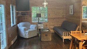 A cozy cabin interior with wooden walls, a sofa, a dining table, and a ceiling fan. - Waterfront Cottage for Rent in Parry Sound Region 
 (Pointe au Baril)