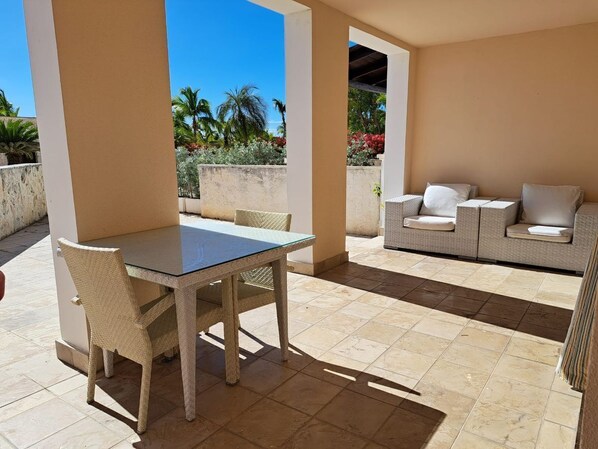 An outdoor patio with a table and chairs, a sofa, and a view of palm trees and flowers.