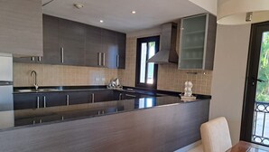 Una cocina moderna con armarios oscuros, una isla grande y una zona de comedor con mesa de vidrio.
