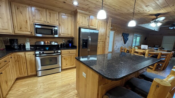 A wooden interior with a kitchen area featuring stainless steel appliances, wooden cabinets, and a central island with seating.
