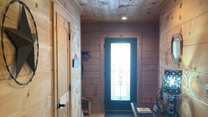 A wooden interior hallway with a star decoration, a door, a desk with a lamp, and a window at the end.