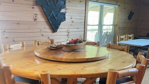 A wooden dining table with chairs, a decorative wall piece, and a window with blinds.