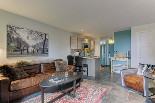 A living room with a brown leather sofa, a coffee table, and a rug. There is a kitchen area with cabinets and a microwave. - The Shores Lake View Condo Unit 5658 (Williamsburg)