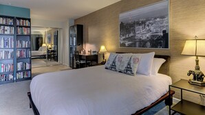 Ein Hotelzimmer mit einem großen Bett, einem Bücherregal, einem Schreibtisch und einem großen Stadtbild an der Wand.