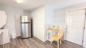 A compact kitchen with a stainless steel refrigerator, a small table with a vase, and wooden flooring. - North MB Beautiful studio across from the beach (North Myrtle Beach)
