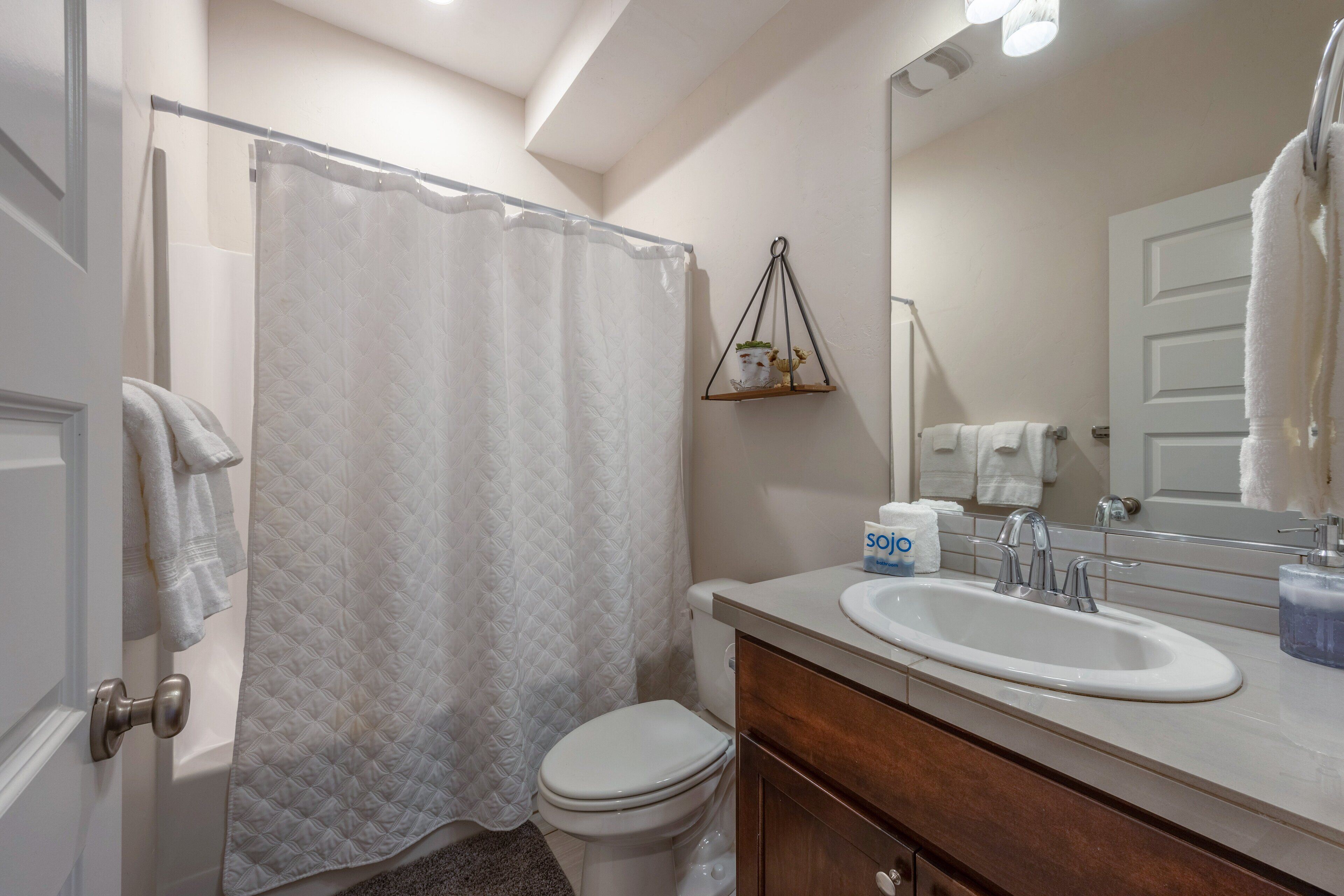 A bathroom with a white toilet, a shower curtain, a sink with a mirror, and a towel rack.