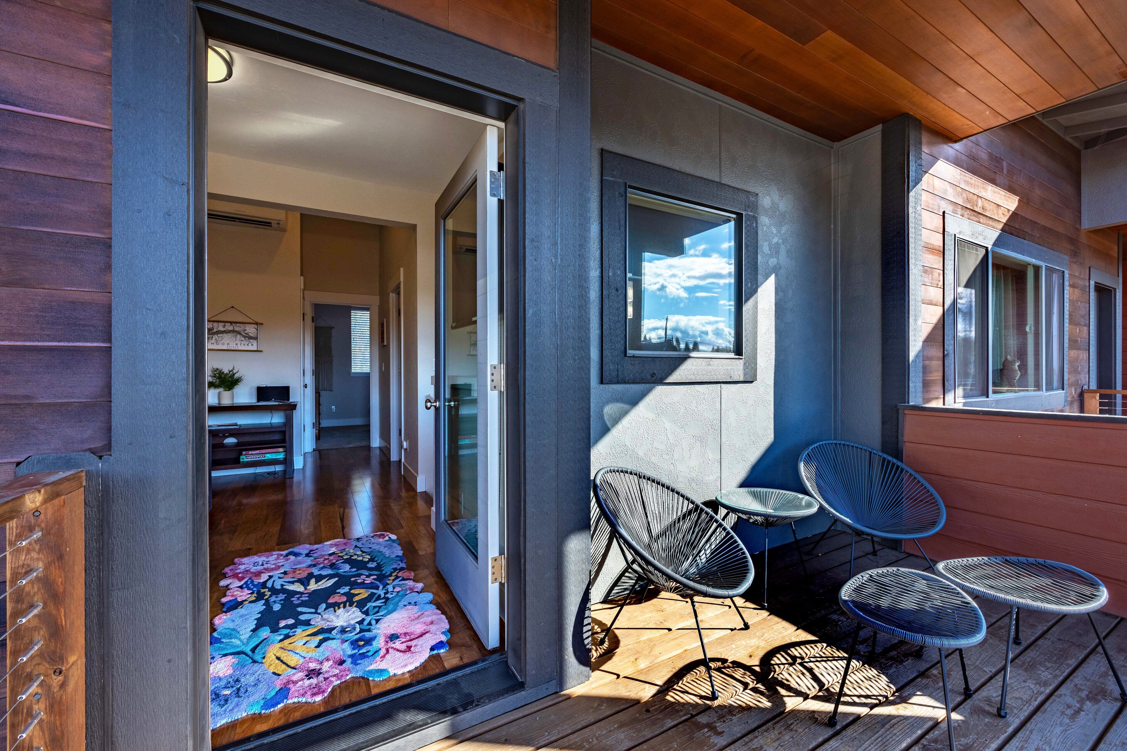 A modern house with a wooden deck, a glass door entrance, and a dining area with metal chairs.