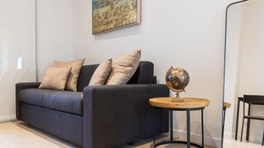 Una sala moderna con un sofá azul oscuro, cojines color beige y una mesita redonda de madera con un globo terráqueo.
