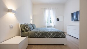 Un dormitorio moderno con cama, mesita de noche y televisor montado en la pared.