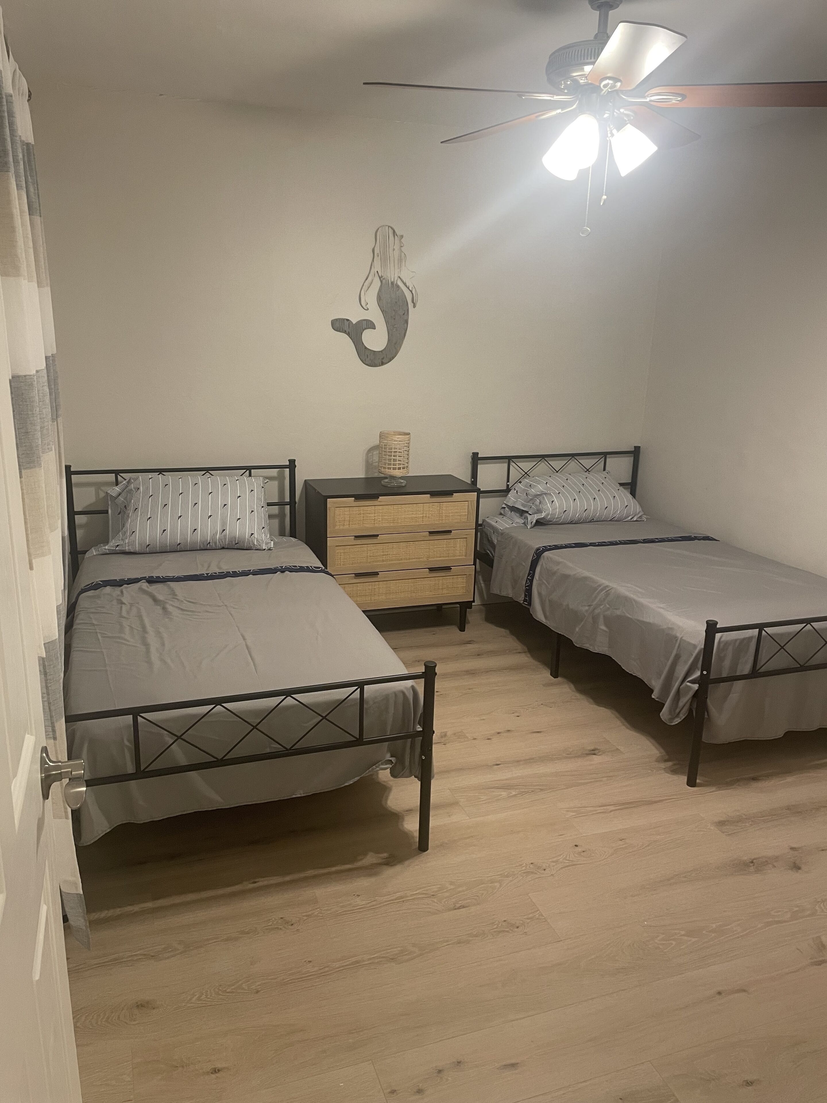 Ein Schlafzimmer mit zwei Einzelbetten, einem Deckenventilator, einem an der Wand befestigten Regal und einem Holzboden.