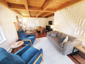 A spacious living area with a wooden ceiling, a grey sofa, blue armchairs, and a small round table.