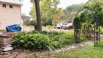 Un jardín con un arco de metal, un objeto cubierto y una casa al fondo.