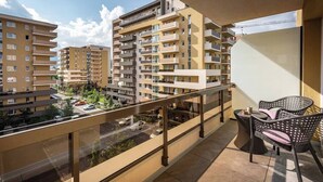 Varanda com vista para edifícios residenciais ao redor, guarda-corpo de vidro e mobiliário de exterior.