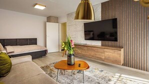 Uma sala de estar moderna com sofá, mesa de centro, televisão fixada em uma parede de madeira e uma cama com cabeceira.