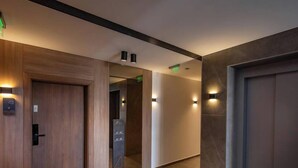 Corredor moderno com portas de madeira, painel digital do elevador e iluminação embutida.