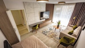 Uma sala de estar moderna com um conjunto de sofás, uma TV fixada em uma parede de mármore e uma mesa de centro pequena com um vaso de flores.