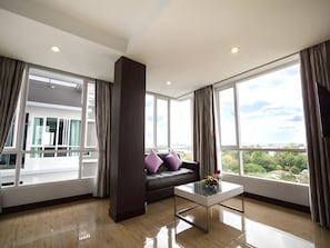 Un salón moderno con un sofá marrón oscuro, una mesa de centro de cristal y grandes ventanales con vistas a un paisaje urbano.