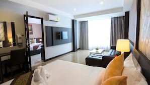 Une chambre d’hôtel avec un lit, un bureau, une télévision, un canapé et une fenêtre avec des rideaux.