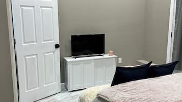 Ein Schlafzimmer mit einem Bett, einem Fernseher auf einem weißen Schrank, einer Tür und einem Fenster.