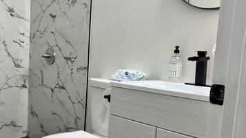 Ein Badezimmer mit Toilette, einer Dusche mit Marmorwand, einem Waschbecken mit Spiegel und einem Schrank mit Schubladen.