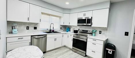 A modern kitchen with white cabinets, a stainless steel dishwasher, a built-in oven, and a microwave.