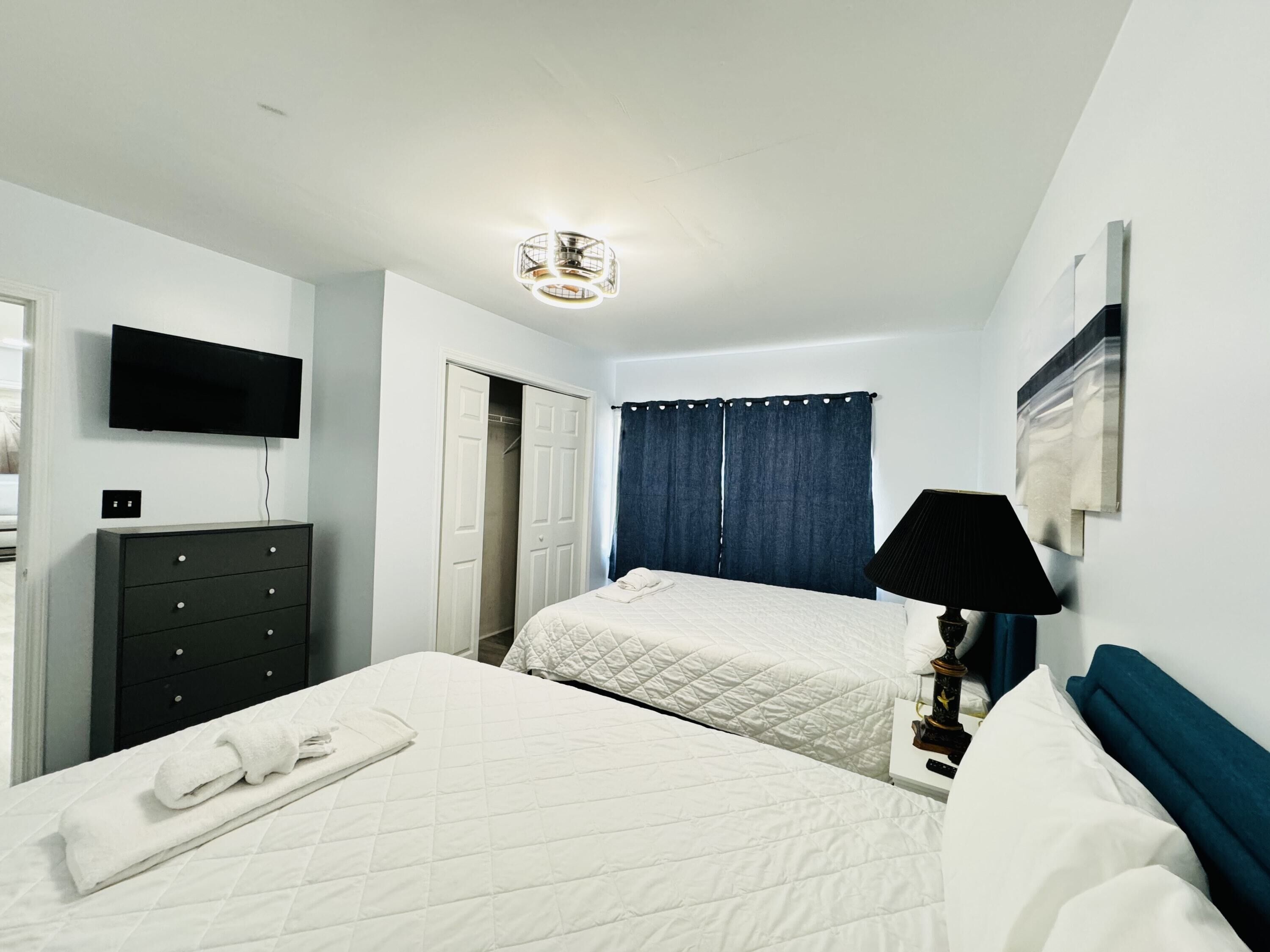 A hotel room with two beds, a TV, a dresser, and a lamp.