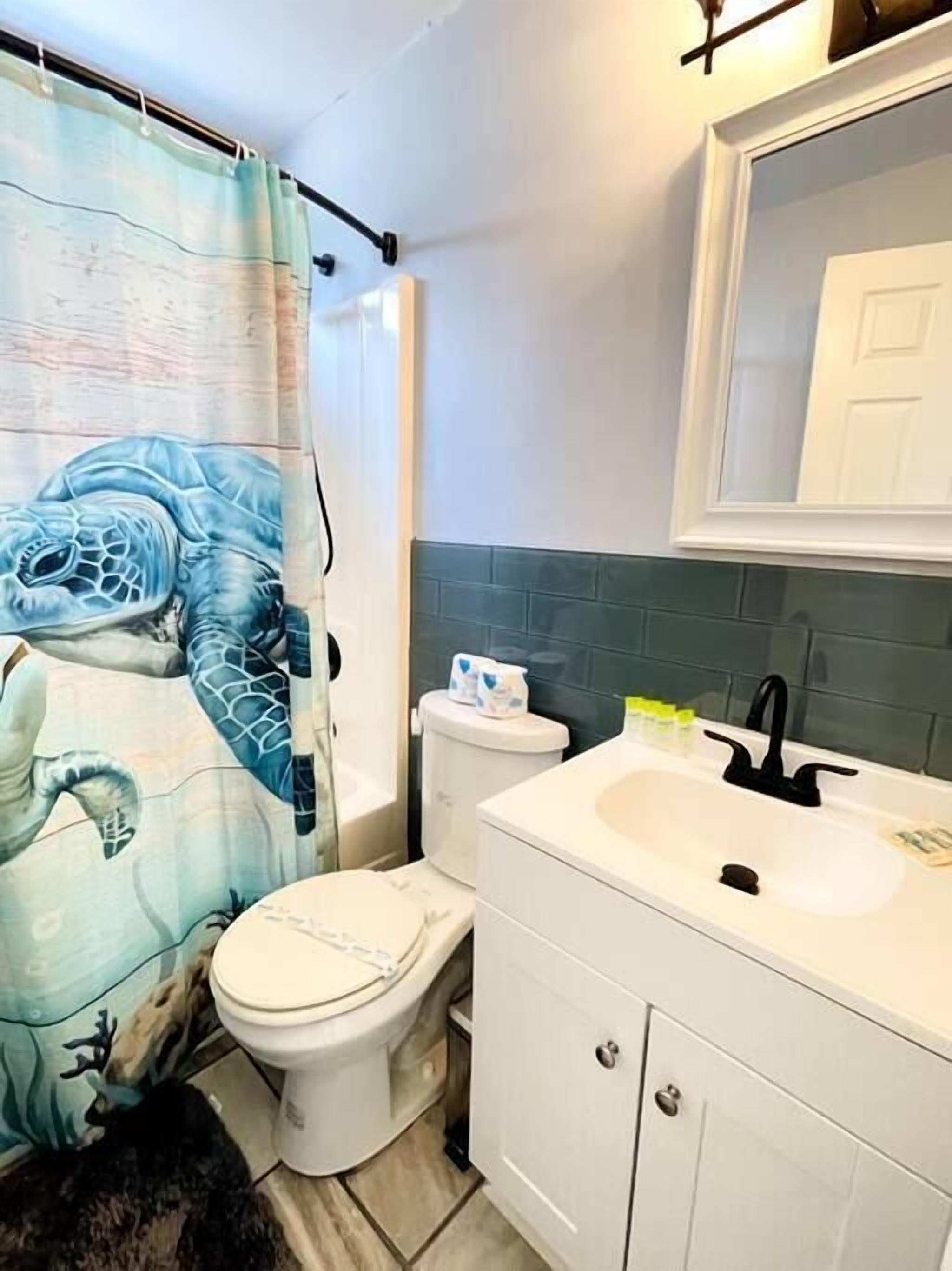 A bathroom with a toilet, sink, and shower curtain featuring a sea turtle design.