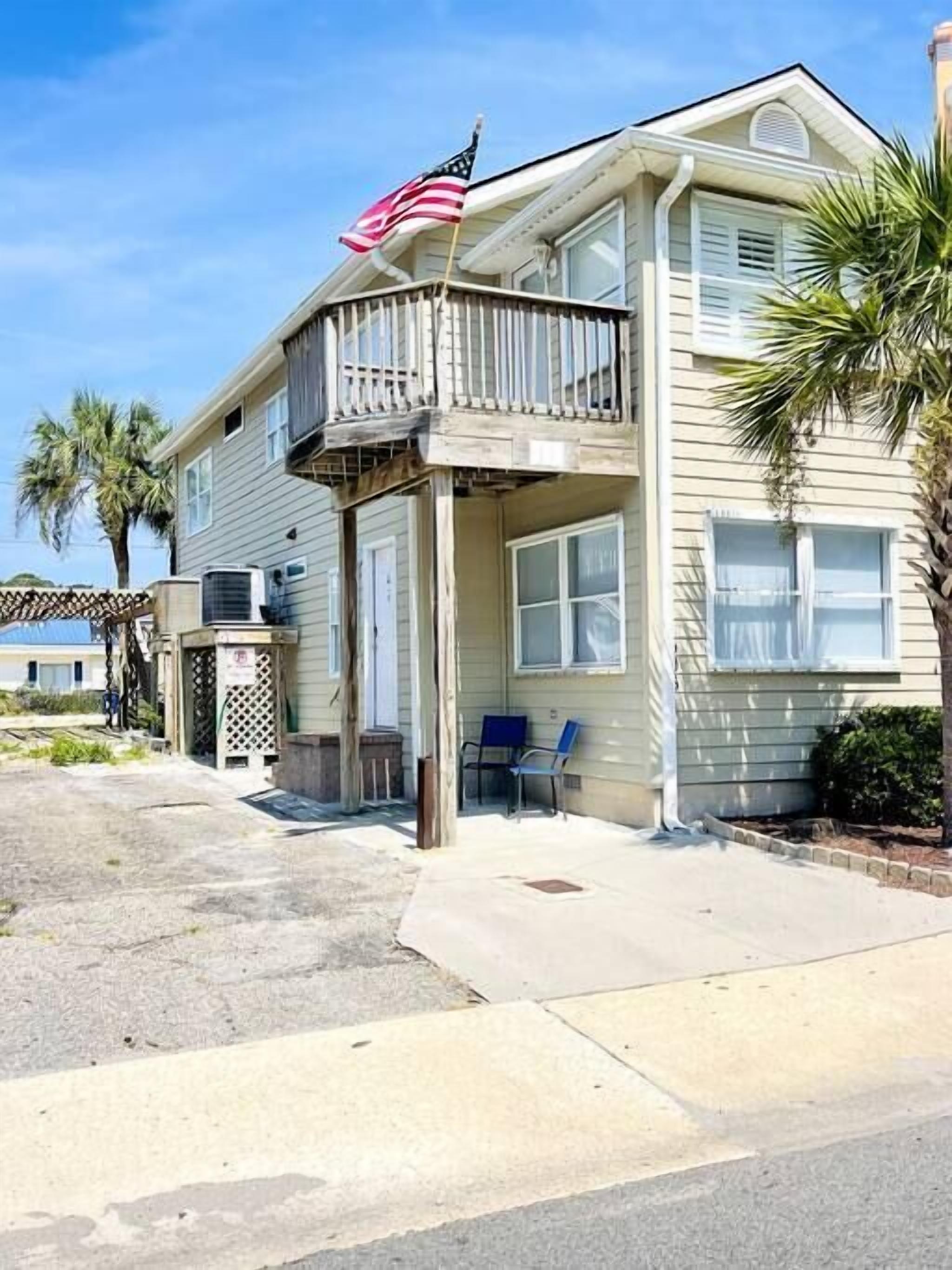 A two-story house with a balcony, an American flag, and a small porch area with chairs.