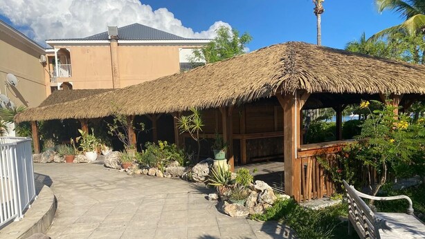 A thatched-roof structure with a wooden bench, surrounded by potted plants and rocks.