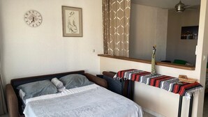 A bedroom with a bed, a bedside table, a clock, a framed picture, and a window with curtains.