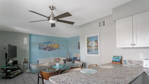 A modern kitchen with a granite countertop, white cabinets, and a ceiling fan. - Oceanfront Condo with Rocket Launch Views - Steps to Beach (Cocoa Beach)