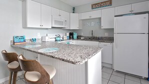 A kitchen with white cabinets, a granite countertop, and a sign that reads "BEACH HOUSE". - Oceanfront Condo with Rocket Launch Views - Steps to Beach (Cocoa Beach)