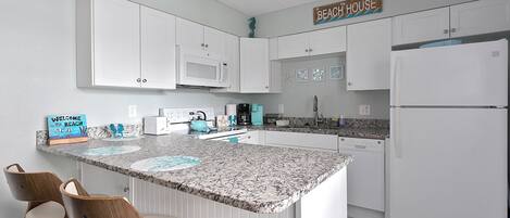 Una cocina con armarios blancos, encimera de granito y un letrero que dice 'BEACH HOUSE'.