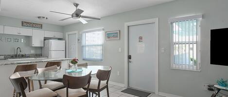 A modern kitchen with white cabinets, a dining area with a glass table and chairs, and a ceiling fan.