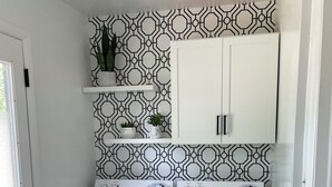 Ein Waschraum mit zwei weißen Waschmaschinen mit Frontlader, einem darüber liegenden weißen Schrank und einer Wand mit Muster.