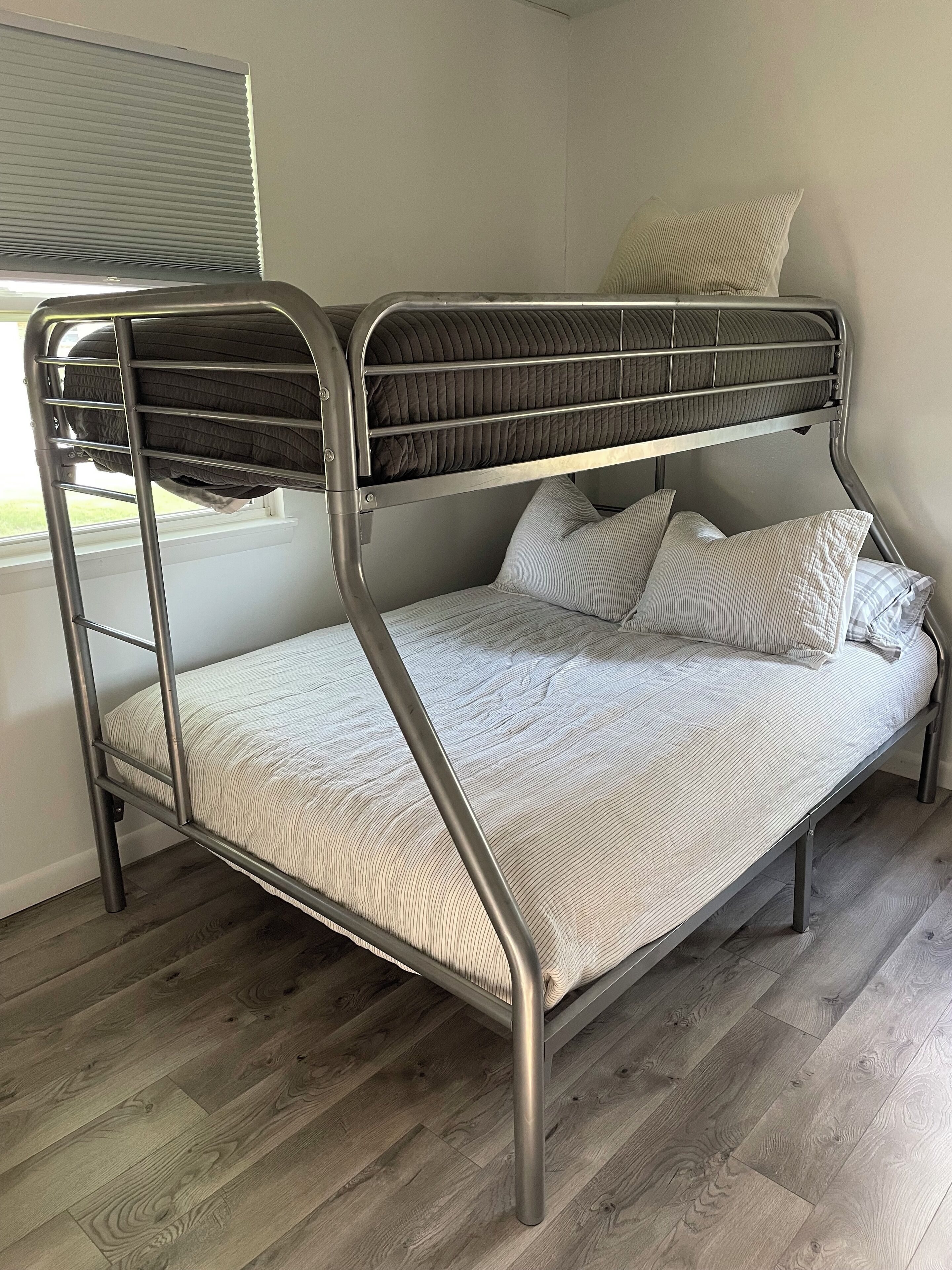 A bunk bed with a metal frame, a lower bed with a striped mattress, and pillows.