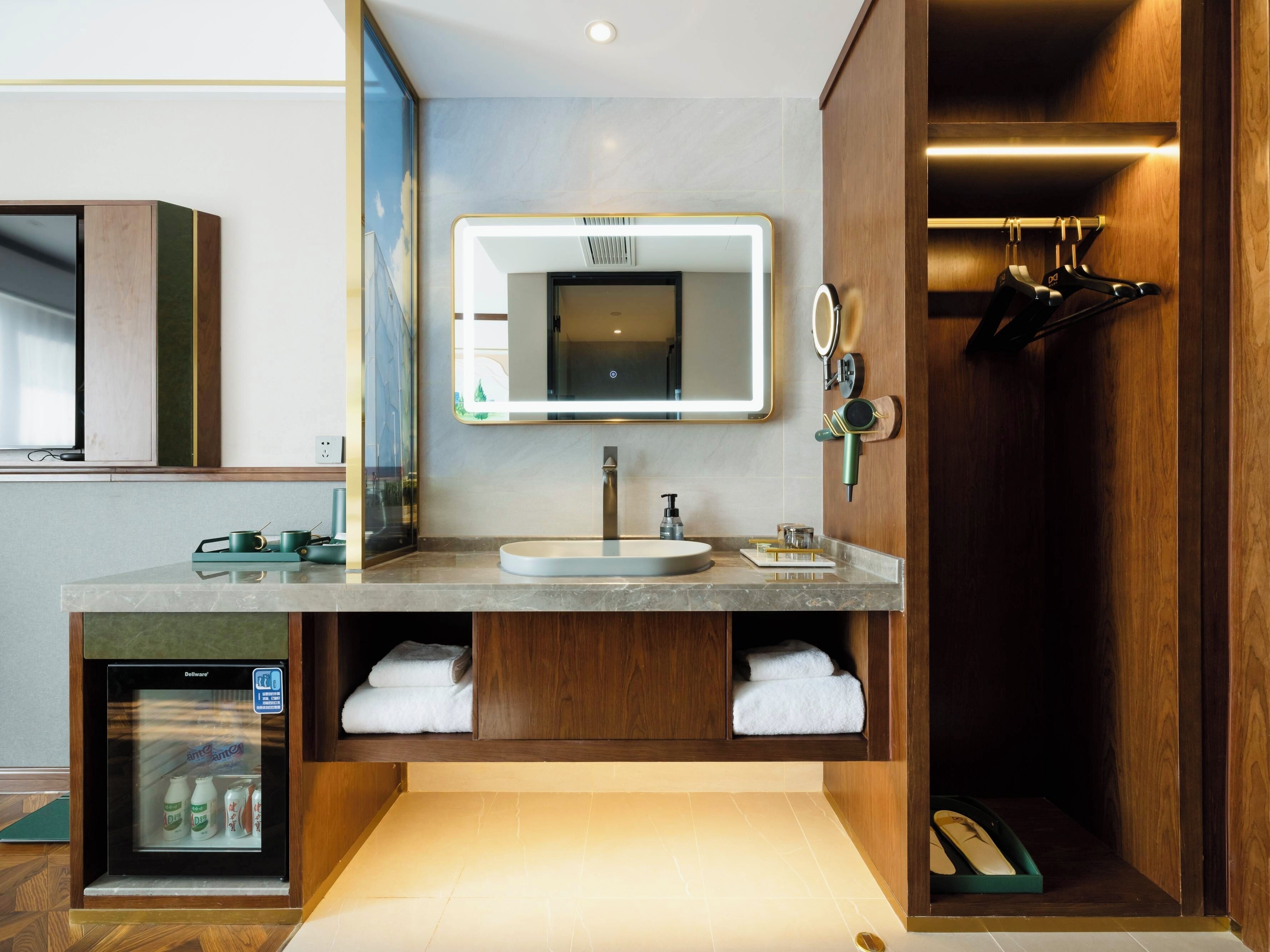 Un baño moderno con lavabo, espejo, toallero y un refrigerador pequeño.