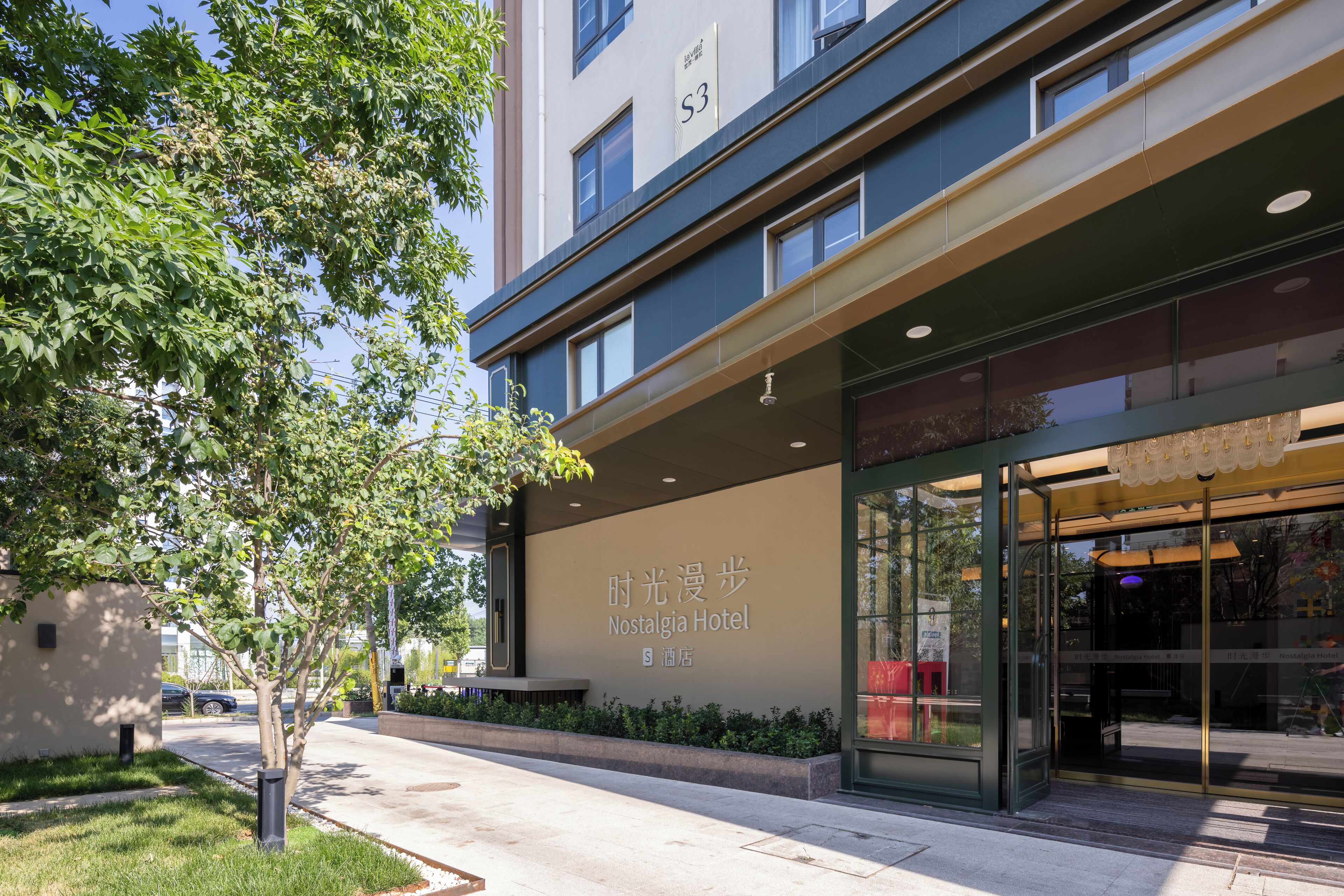 A modern hotel entrance with a large sign, a tree-lined sidewalk, and a clear view of the building's facade.