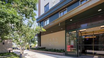 A modern hotel entrance with a large sign, a tree-lined sidewalk, and a clear view of the building's facade.